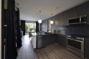 Une cuisine moderne avec des meubles de couleur sombre, des appareils en acier inoxydable et des luminaires suspendus.
