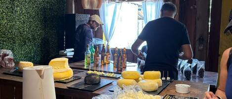 A rustic interior with wooden beams, a green wall, and a bar area with cheese and bottles.