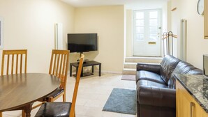 Ein Wohnzimmer mit Esstisch, Stühlen, Fernseher, Sofa und einer Tür mit Fenster.
