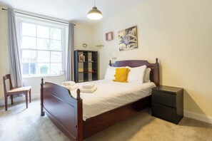 A bedroom with a bed, a nightstand, a chair, a window, and a bookshelf.
