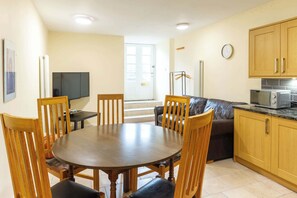 A dining area with a round table and chairs, a sofa, a television, and a kitchen with cabinets and a microwave.