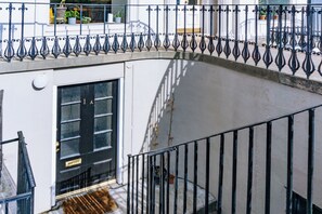 A balcony with a black metal railing, a white wall, and a black door with a window.
