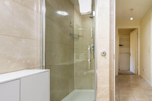 A modern bathroom with a glass-enclosed shower, a white bathtub, and a walk-in closet with shelves.