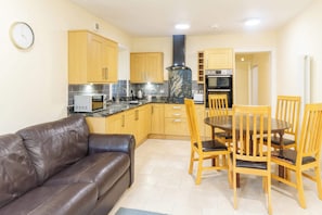 A compact kitchen with wooden cabinets, a black stove, and a dining area with wooden chairs.