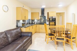 A compact kitchen with wooden cabinets, a black stove, and a dining area with wooden chairs.