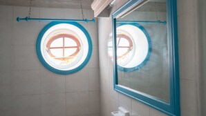 A bathroom with a round window, a mirror, and a towel rack.