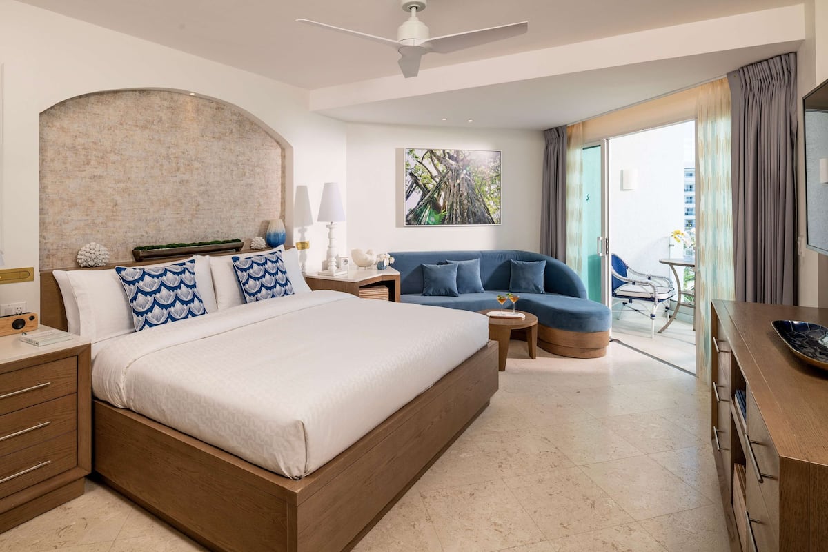 Ein modernes Hotelzimmer mit einem großen Bett, einer Sitzecke, einem Essbereich und einem Balkon mit Blick.
