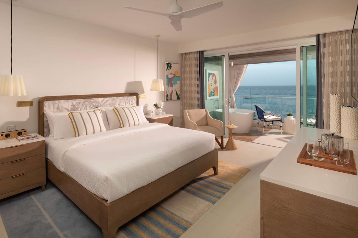 Ein modernes Hotelzimmer mit einem großen Bett, einem Schreibtisch und einem Balkon mit Meerblick.