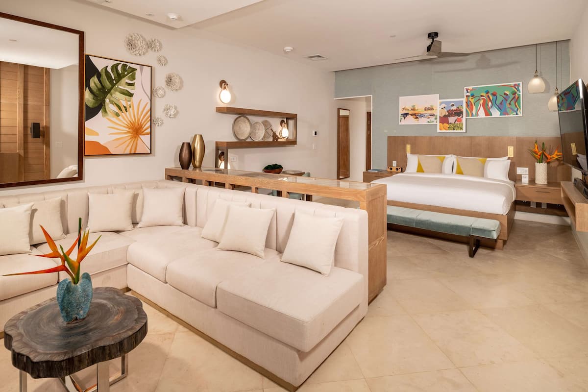 Ein modernes Hotelzimmer mit einer großen Couch, einem Bett, einem Holznachttisch und einem kleinen runden Tisch mit einer Vase.