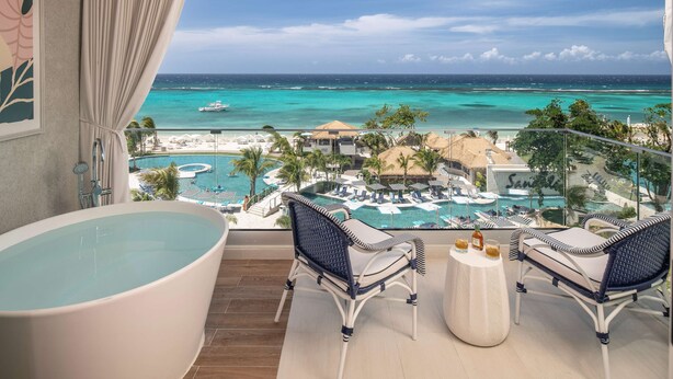 A balcony with a view of a beach resort, including a pool area and a large bathtub. - Sandals Dunns River - All-inclusive Adults Only (Ocho Rios)