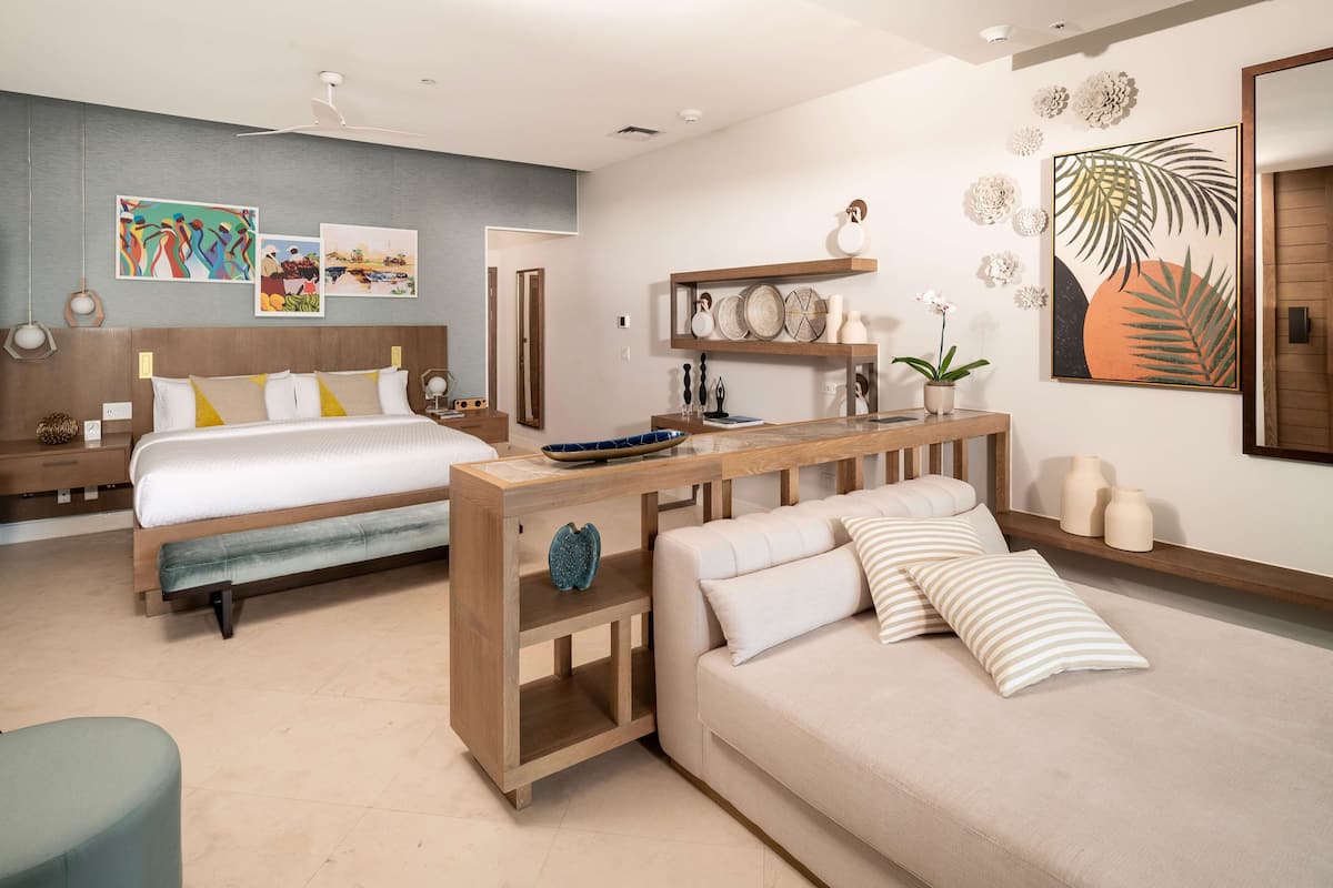 Ein modernes Schlafzimmer mit einem großen Bett, einer Couch und einem Holznachttisch. An den Wänden befinden sich Kunstwerke und Dekorationselemente.