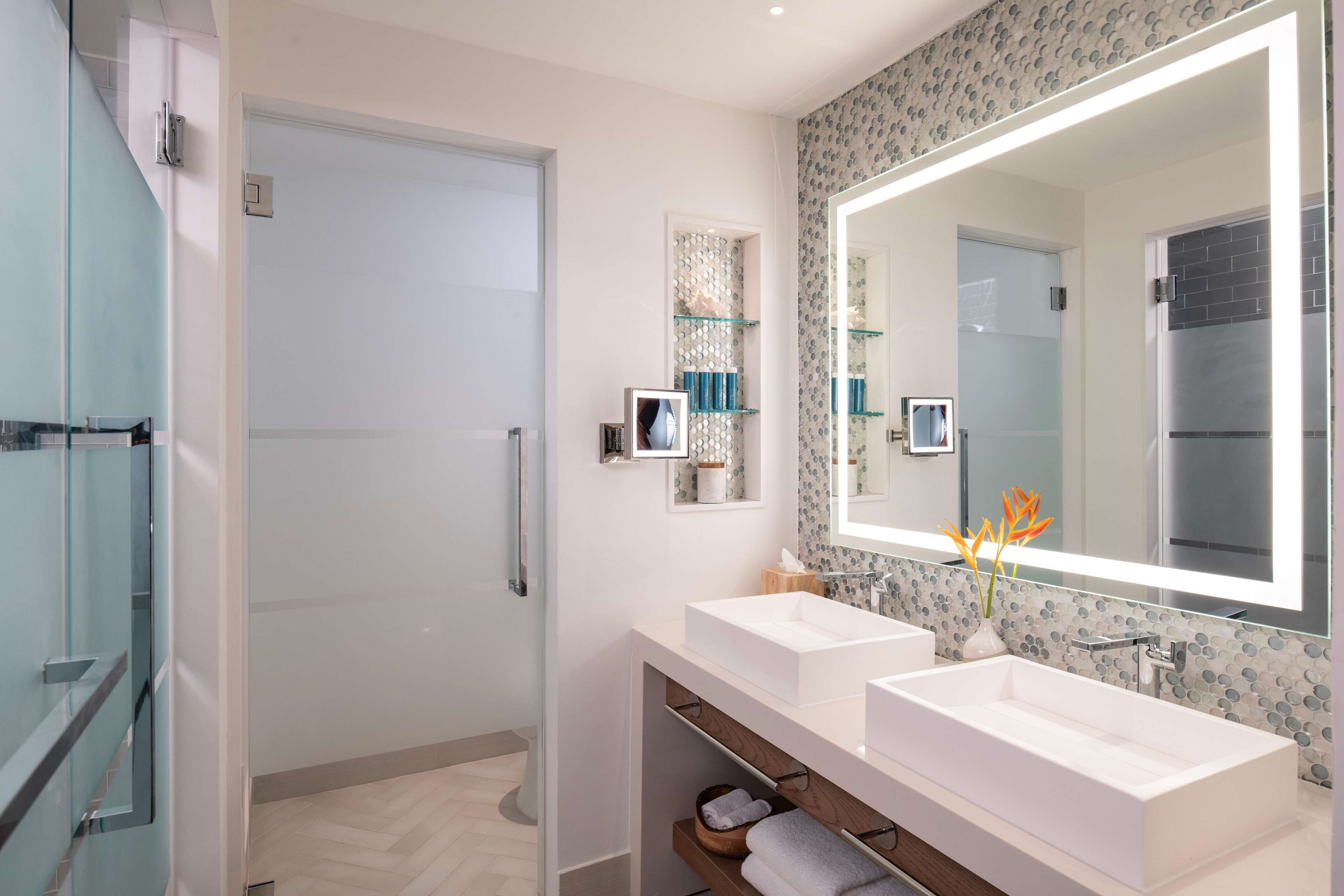 A modern bathroom with two sinks, a large mirror, and a shower area.