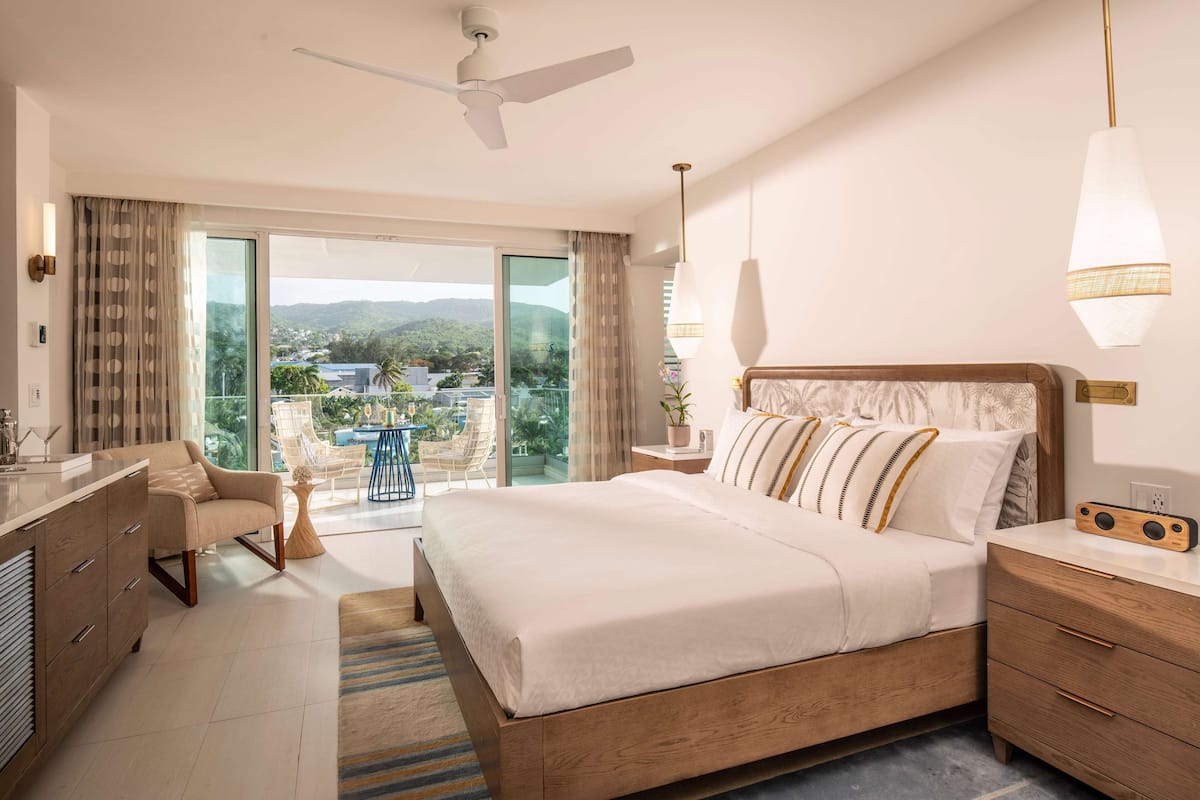 Ein Hotelzimmer mit einem großen Bett, einem Schreibtisch, einem Stuhl, einem Deckenventilator und Blick ins Freie.