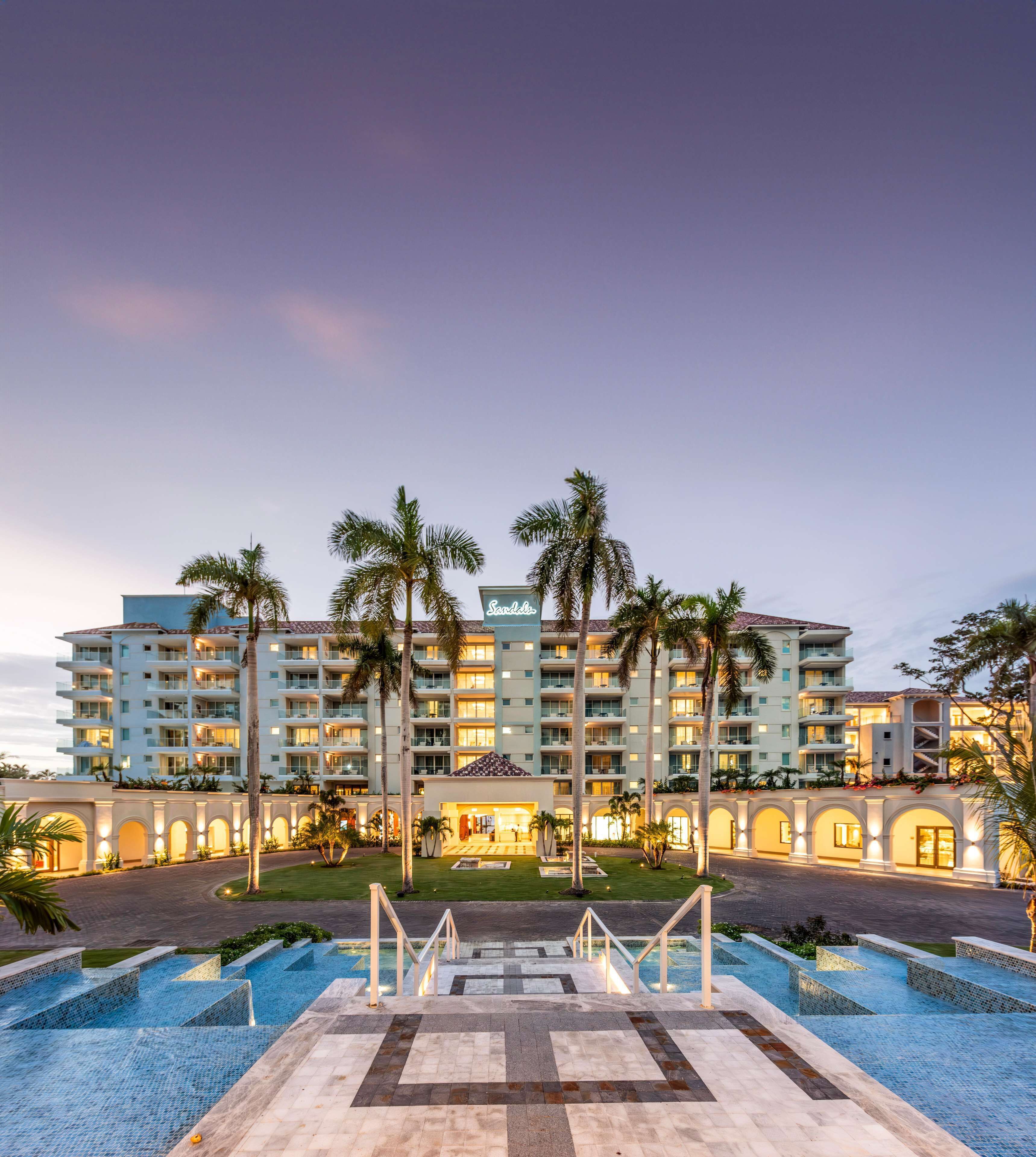 A hotel with multiple floors, a swimming pool, and palm trees.