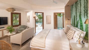 Una habitación de hotel moderna con una cama grande, una zona de estar con sofá y sillón, una televisión y vistas a una piscina y área exterior.