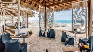 Un restaurante frente a la playa con terraza, techo de paja y vistas al mar.