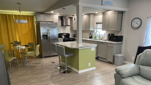 A modern kitchen with a central island, bar stools, and a dining area with a yellow curtain. - Beautiful 55+ Senior Gated Oasis: Pool, Pickleball & Small Pets Welcome! (punta gorda)