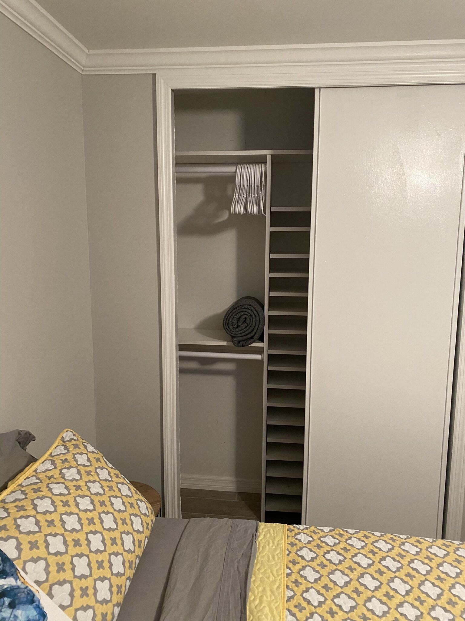 A bedroom with a bed, a closet with hanging clothes, and a folded blanket on the floor.