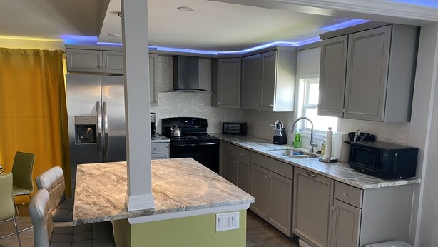 A modern kitchen with grey cabinets, a stainless steel refrigerator, a black stove, and a microwave. - Beautiful 55+ Senior Gated Oasis: Pool, Pickleball & Small Pets Welcome! (punta gorda)