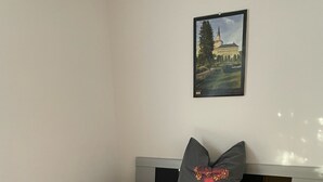 A bed with a grey blanket and pillows, a framed picture on the wall, and a tiled floor. - Small vacation apartment in Bad Lauchstädt (Goethestadt Bad Lauchstädt)