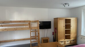 A room with bunk beds, a television, a wooden cabinet, and a crib.