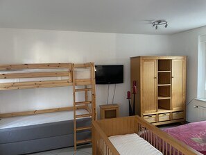 Ein Zimmer mit Etagenbetten, einem Fernseher, einer Holzkommode und einem Babybett.