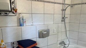 A bathroom with a sink, toilet, and bathtub. There are toiletries on the sink and a trash can next to the toilet.