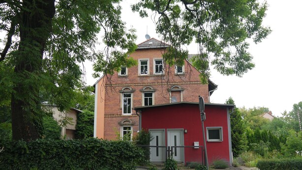 A red building with a brick facade, multiple windows, and a small attached structure.