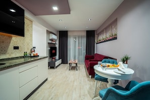 En moderne stue med et fjernsyn, et spisebord med et fad frugt, en rød sofa og en blå lænestol.