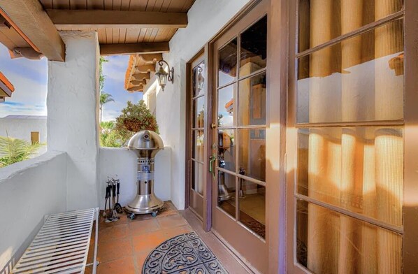 A patio with a grill, a metal bench, and a door with glass panels.