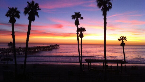 A beach scene with palm trees and a pier at sunset. - Experience San Clemente's Historic Charm in Our Beautifully Furnished Studio (San Clemente)