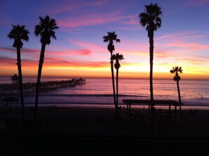 A beach scene with palm trees and a pier at sunset.