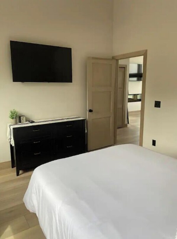 Une chambre à coucher avec un lit, une commode, un téléviseur fixé au mur et une porte donnant sur un balcon.