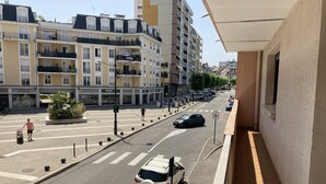 A street view with a white car parked on the side, a pedestrian crossing, and buildings with balconies and storefronts.