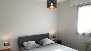 A neatly made bed with two pillows, a bedside lamp, and a blanket on the floor.