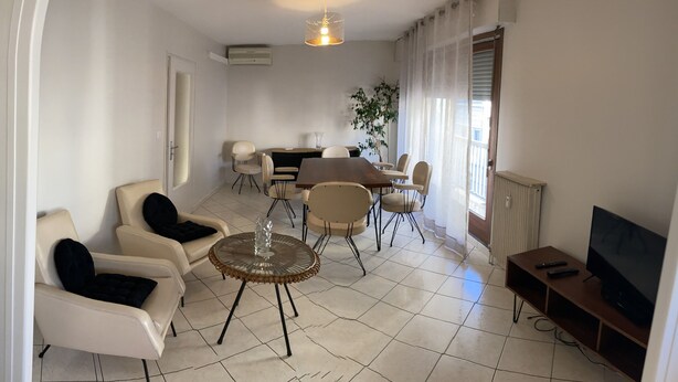 A modern living room with a sofa, armchair, dining table, chairs, a TV, and a radiator.