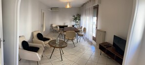 Una sala moderna con sofá, sillón, mesa de comedor, sillas, televisor y radiador.