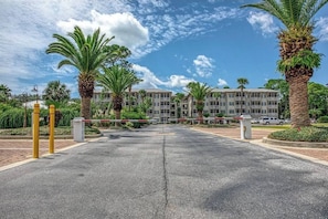 A gated entrance to a multi-story building with palm trees and a clear sky.