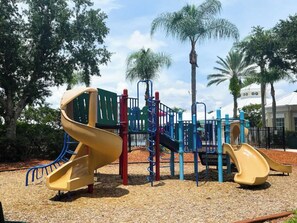 Ein Spielplatz mit Rutschen und Klettergerüsten, umgeben von Bäumen und einem Gebäude im Hintergrund.