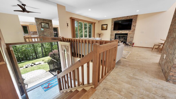 A spacious living room with a fireplace, a large TV mounted on the wall, and a balcony with a wooden railing.