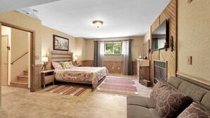 A bedroom with a bed, nightstands, a dresser, a mirror, a fireplace, a sofa, and a window with curtains.