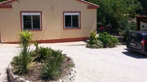 A single-story building with a beige facade and red trim, featuring two windows and a small garden area with desert plants. - House with swimming pool in the pines 500M from the sea (MARTIGUES)