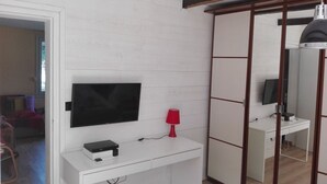 A room with a white desk, a flat-screen TV mounted above it, a red lamp, and a sliding wardrobe. - House with swimming pool in the pines 500M from the sea (MARTIGUES)