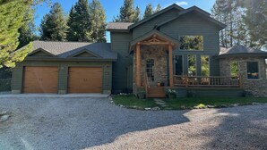A two-story house with a stone porch, a small deck, and a garage. - Cozy mountain retreat with a hot tub; steps to national forest trails! (Alpine)