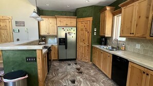 A kitchen with wooden cabinets, a stainless steel refrigerator, and a tiled floor with footprints. - Cozy mountain retreat with a hot tub; steps to national forest trails! (Alpine)