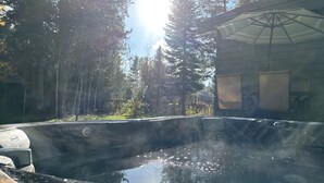 A hot tub in a natural setting with a view of trees and a building in the background. - Cozy mountain retreat with a hot tub; steps to national forest trails! (Alpine)