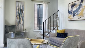 Ein modernes Wohnzimmer mit einem grauen Sofa, zwei grauen Sesseln, einem Couchtisch und einer Treppe.
