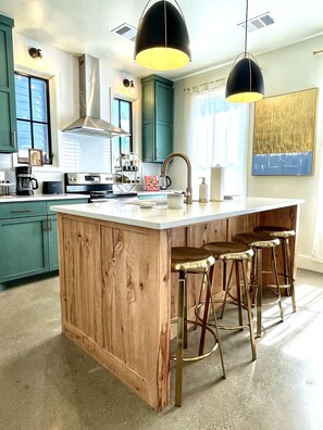 A kitchen with a central island, bar stools, and a large window. - Modern Luxury in Wheeler District • Walk to Dining, Parks & Coffee (Oklahoma City)