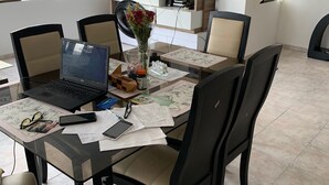 A dining area with a glass table, black chairs, a laptop, and a vase with flowers.