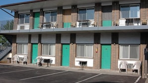 Un motel de dos pisos con una puerta verde, un balcón con sillas y un estacionamiento.